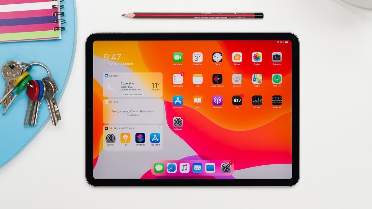 A modern iPad on a white desk displaying the iPadOS home screen