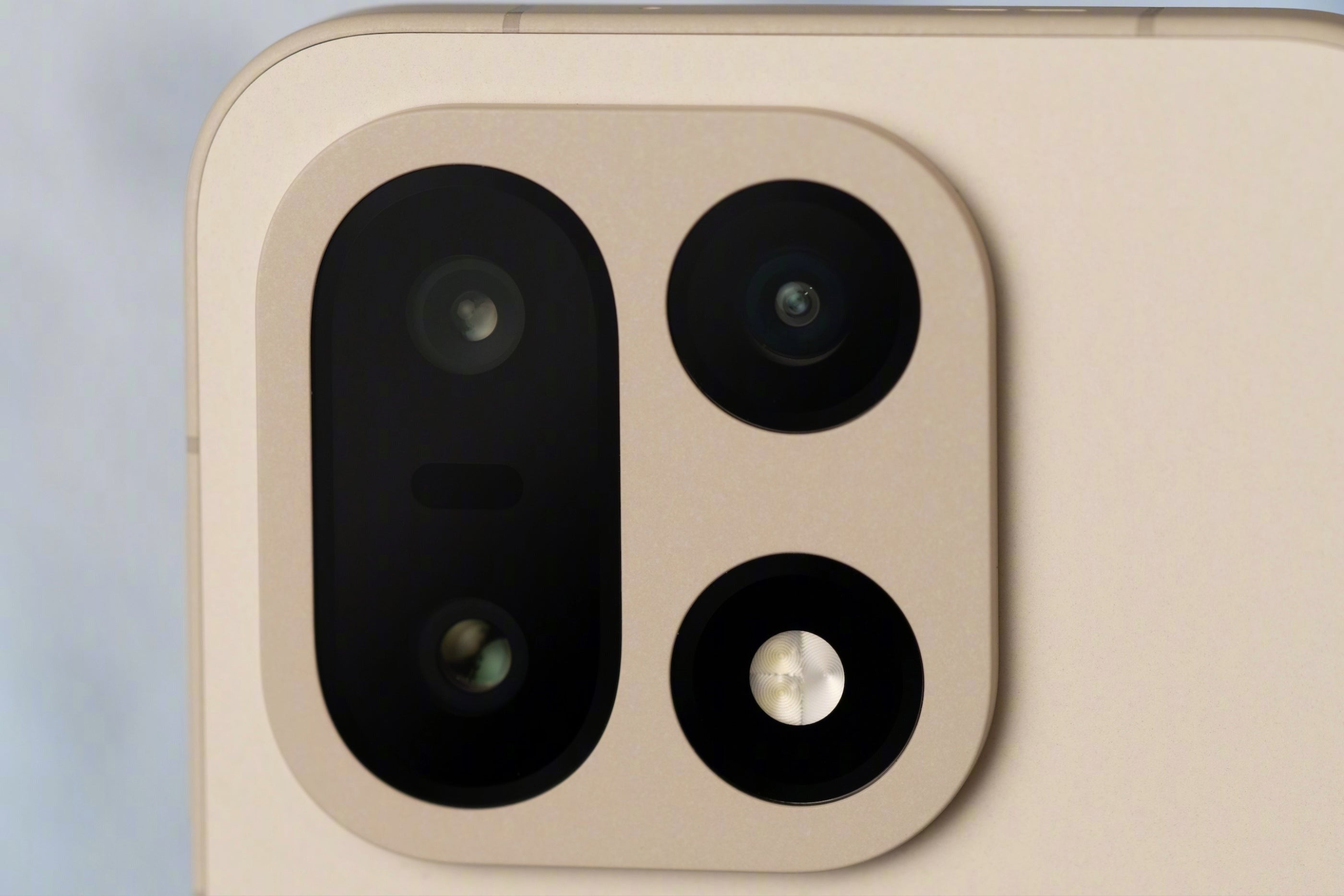 A close-up of the OnePlus 15’s beige rear camera housing, showing its triple-lens setup and LED flash in detail.