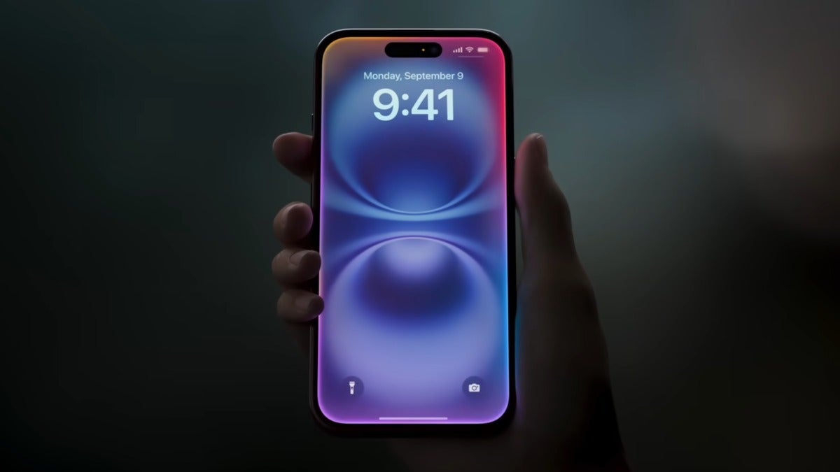 Hand holding an iPhone with a glowing, colorful lock screen in a dark setting.