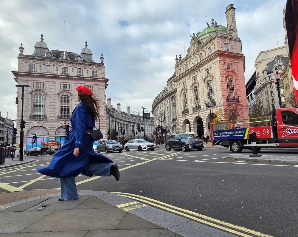 A woman in the streets of London with cars behind her.