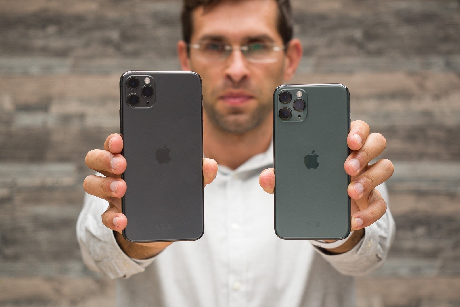 Person holding two iPhone 11 Pro units side by side, showing their back cameras.