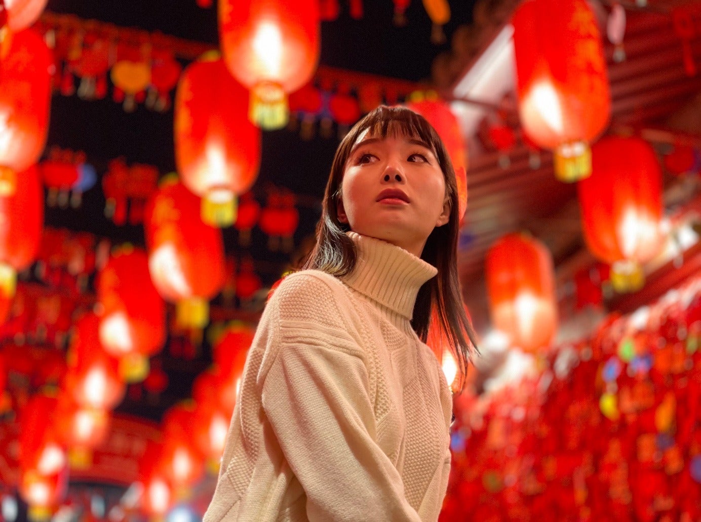 Woman in a white sweater under bright red lanterns at night.