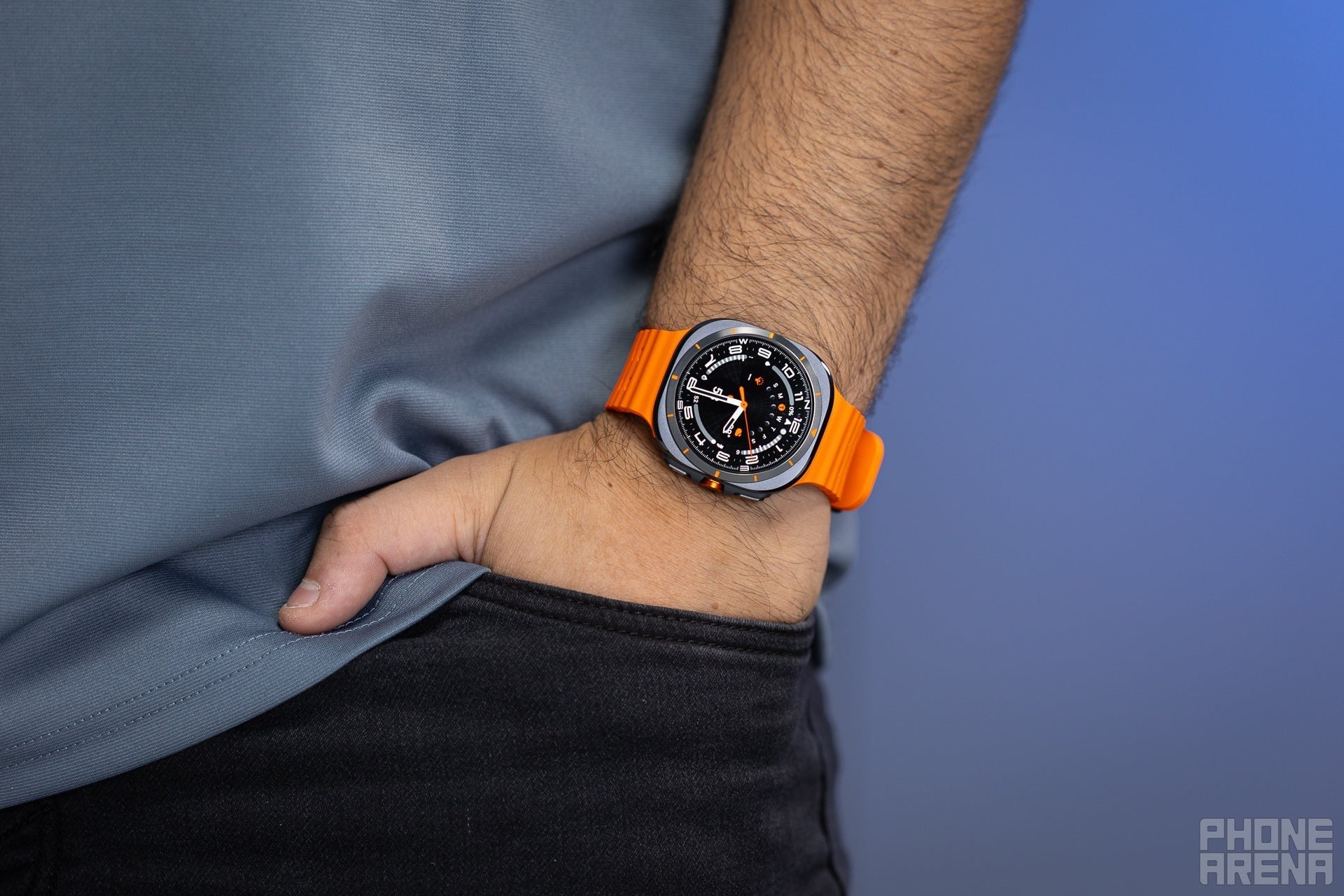Samsung Galaxy Watch Ultra with orange band on wrist, hand in pocket