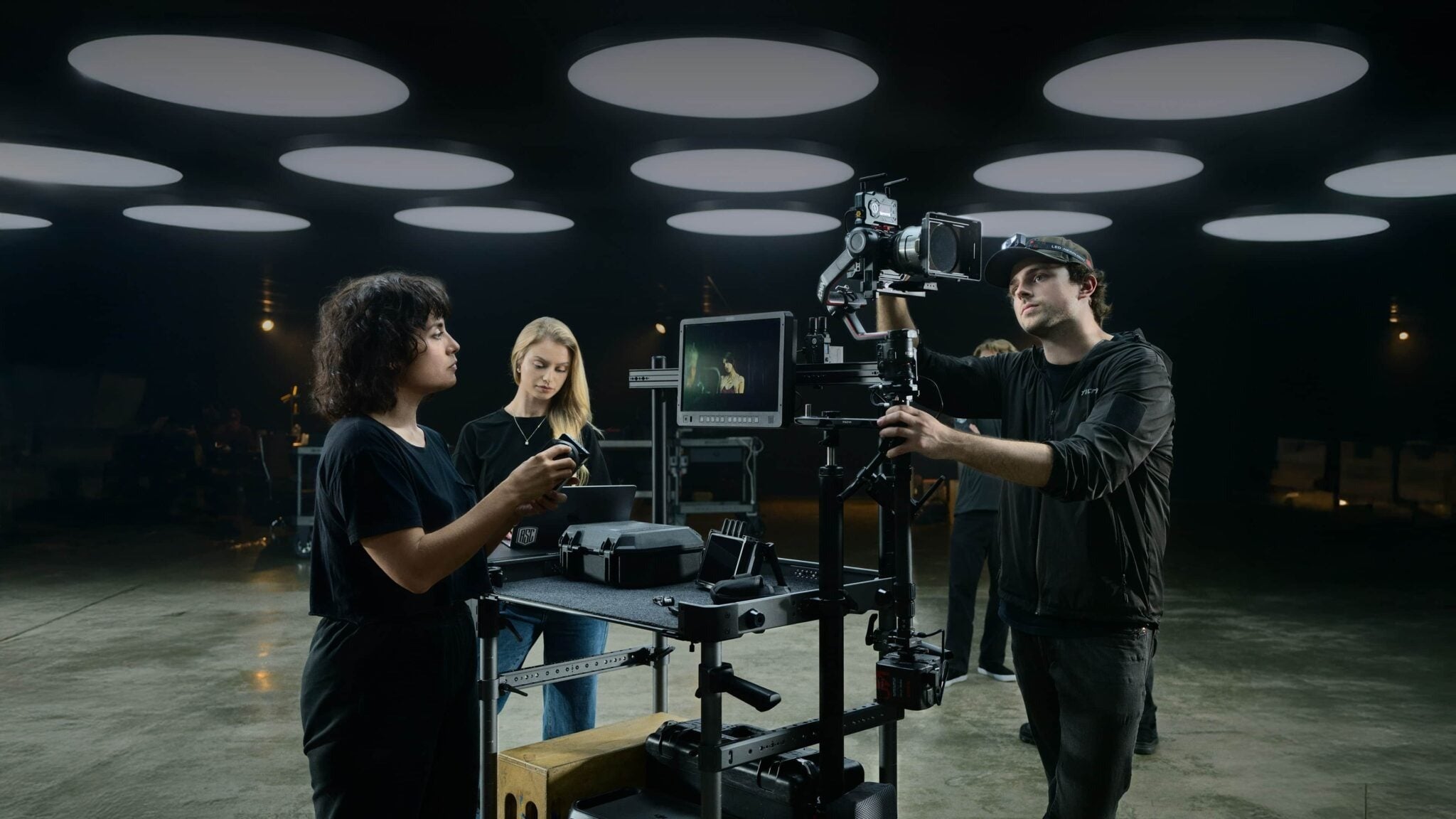 Film crew setting up a professional cinema camera rig in a dark studio with circular ceiling lights.