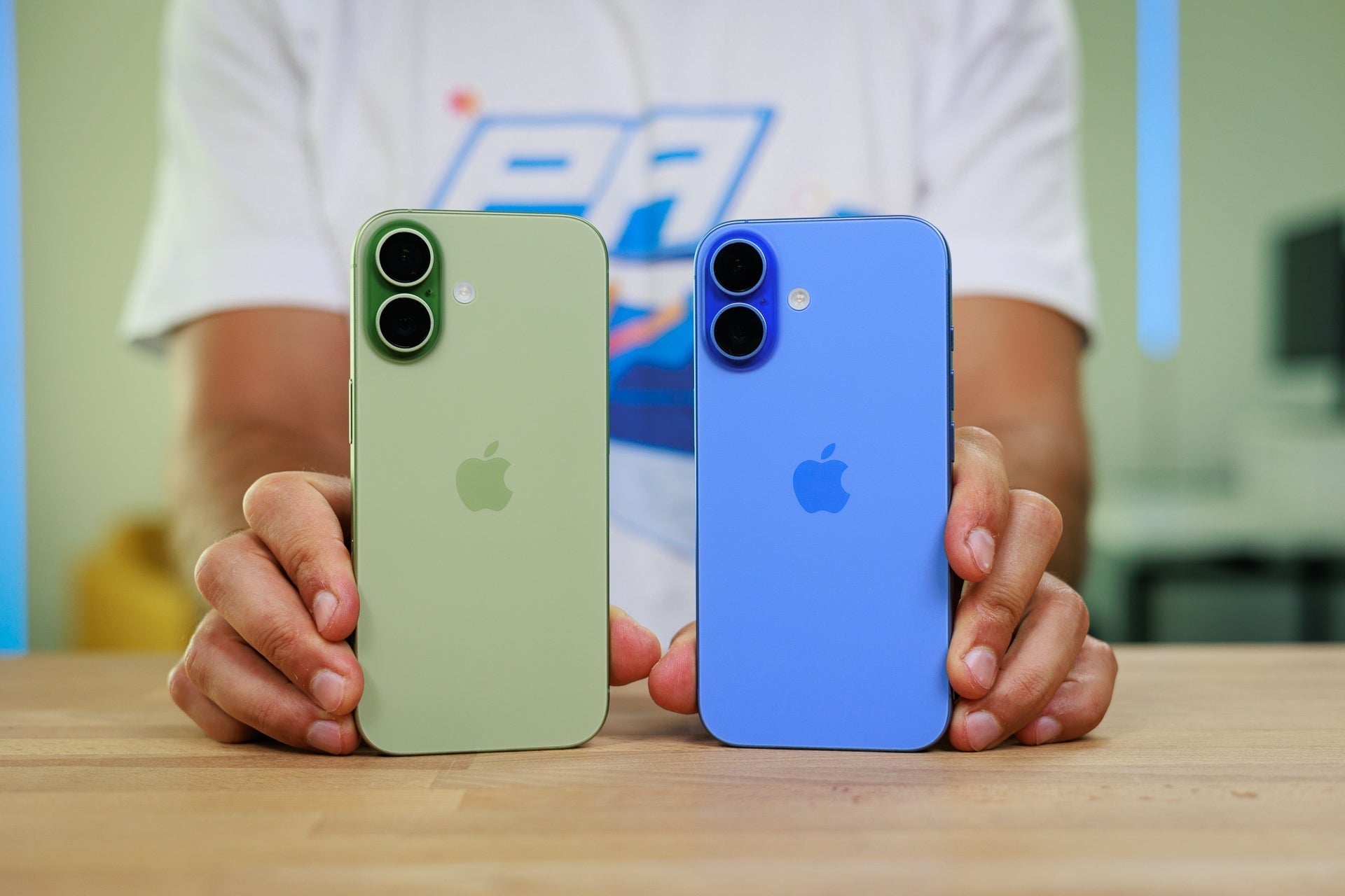 Two iPhones in green and blue colors held side by side, showing dual-camera designs and matte glass backs.