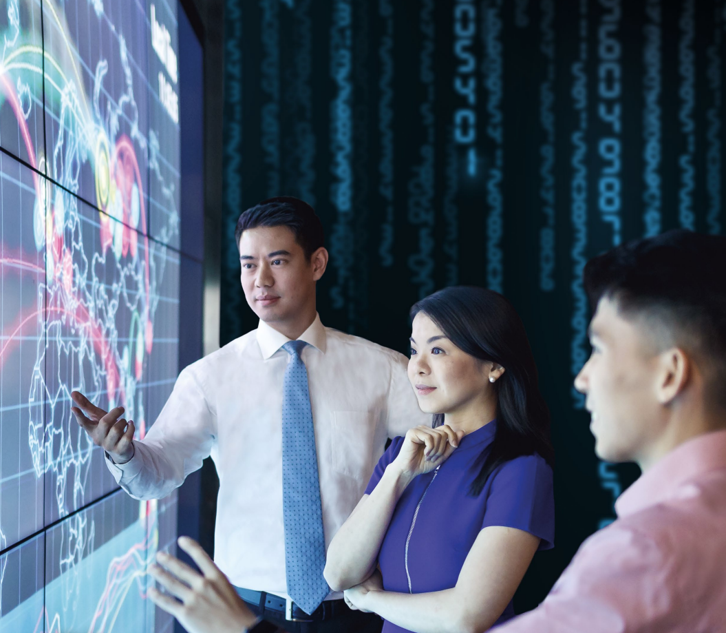 Three people close to a large screen with data figures on it.