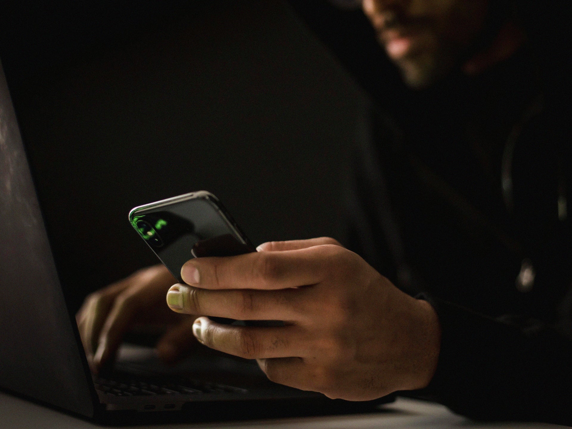 Man holding phone while working on a laptop.