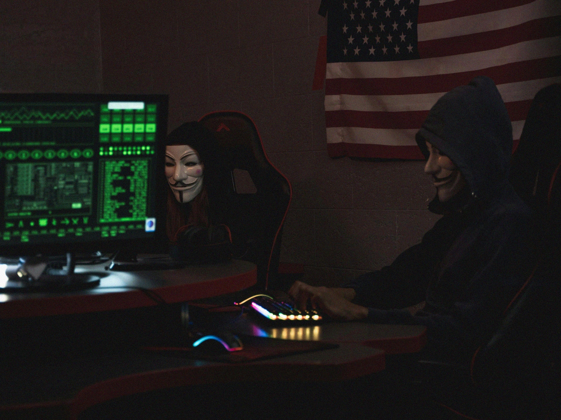 Men with masks working on laptops in dark room.