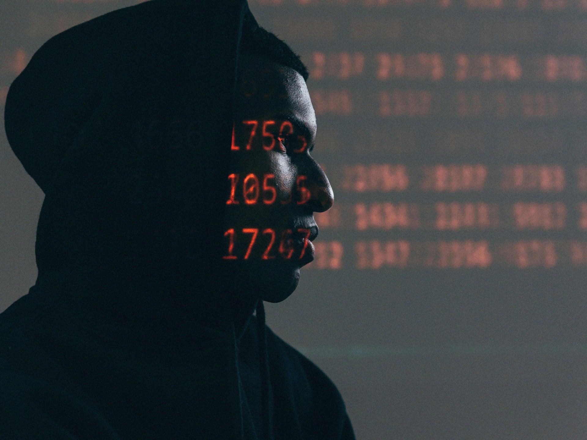 Man with dark hood with red numbers over face.