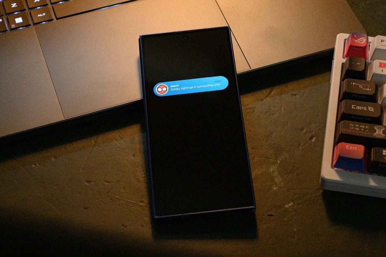 A Samsung Galaxy phone on a desk showing a Spidey Tracker alert about Spider-Man sightings nearby.