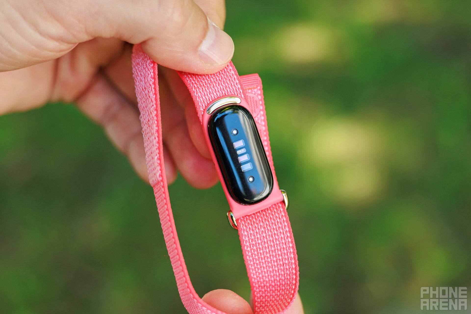 A hand holds up the pink Fitbit Air band, turned to show the black sensor module and heart rate sensors on the underside of the screenless tracker.