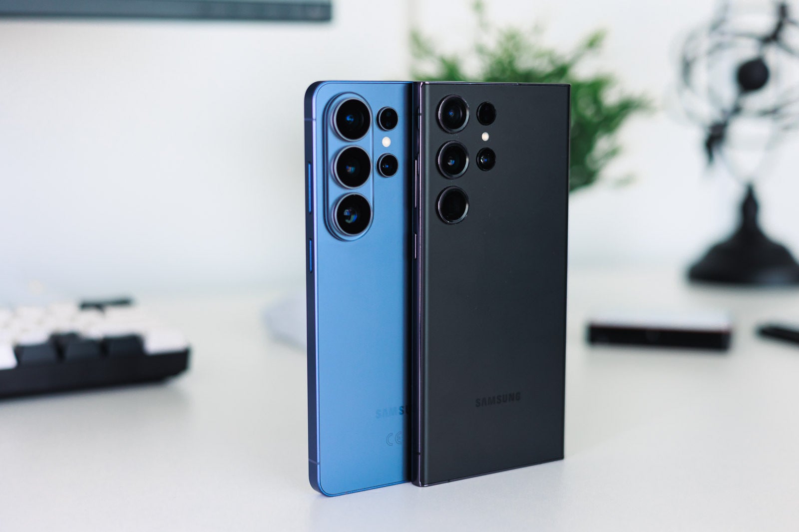 A blue and a black Galaxy S Ultra phones on a desk close to each other..