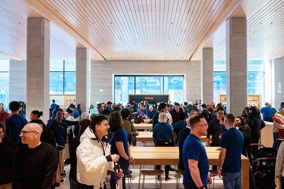 Wide interior view of an Apple Store showing product tables and wood fixtures.