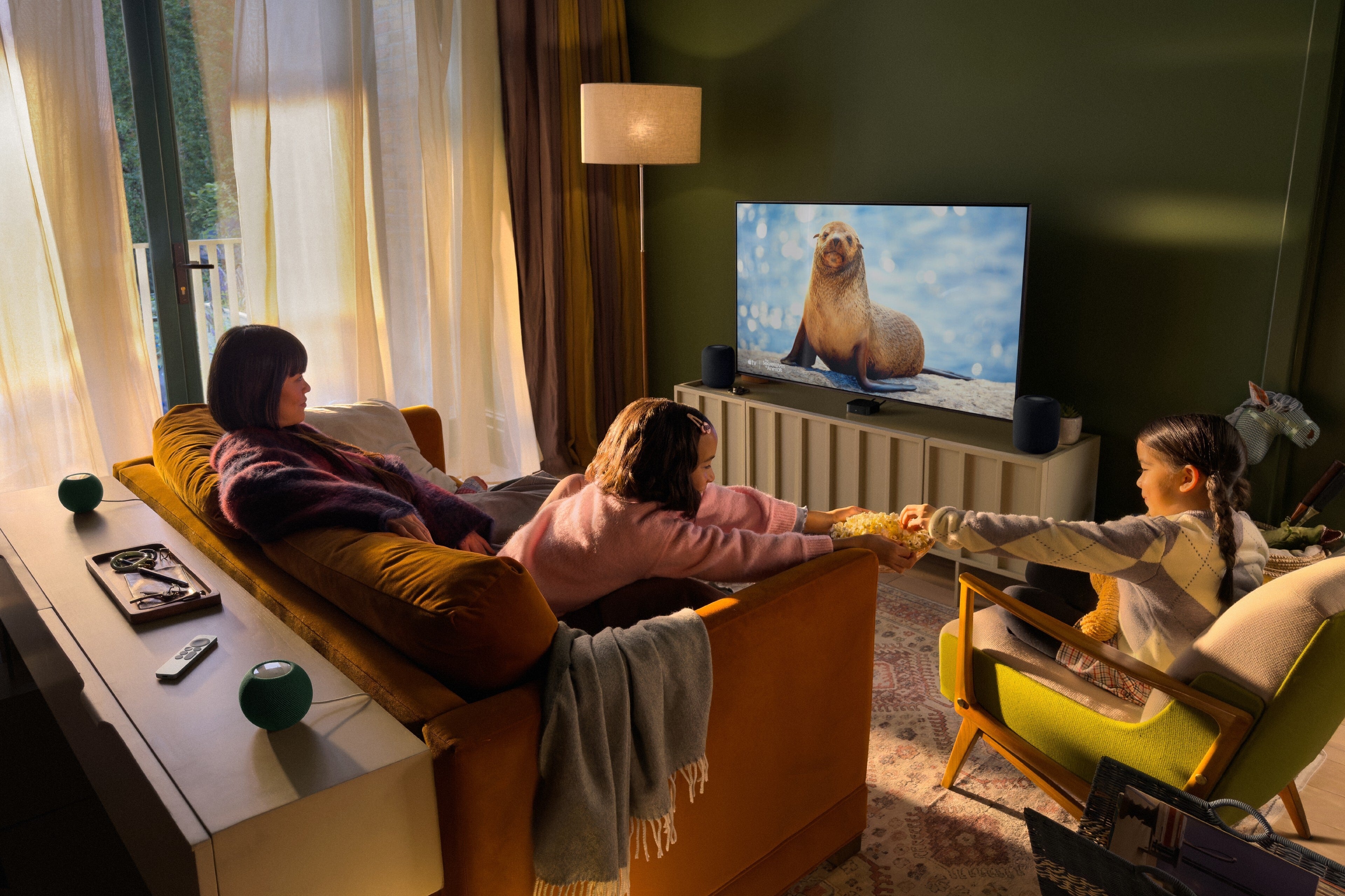Family watching Apple TV 4K with four HomePod mini speakers