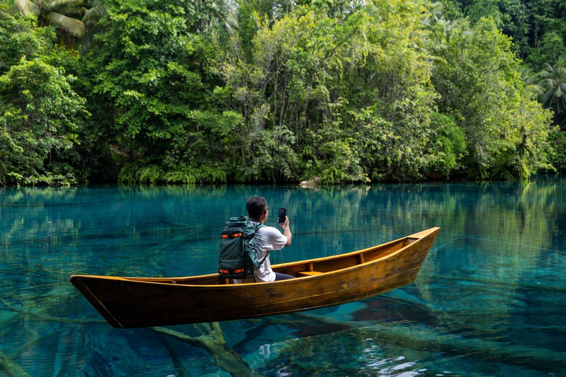 Man in a canoe using a phone on a remote lake
