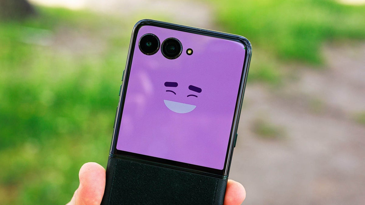 A foldable phone with a purple cover screen showing a smiling emoji face.