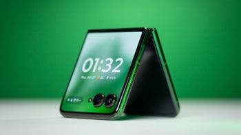 A flip phone sitting face down like a tent on a table, with a green background.