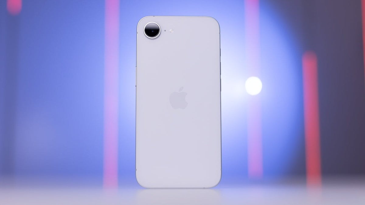 White iPhone 16e standing upright on a surface, with a blurred purple and pink light background.