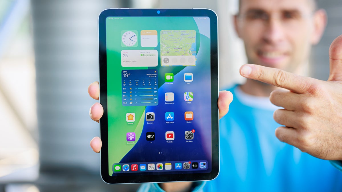 Person holding iPad mini towards the camera, screen is on, showing the homescreen