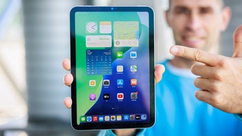 Person holding iPad mini towards the camera, screen is on, showing the homescreen