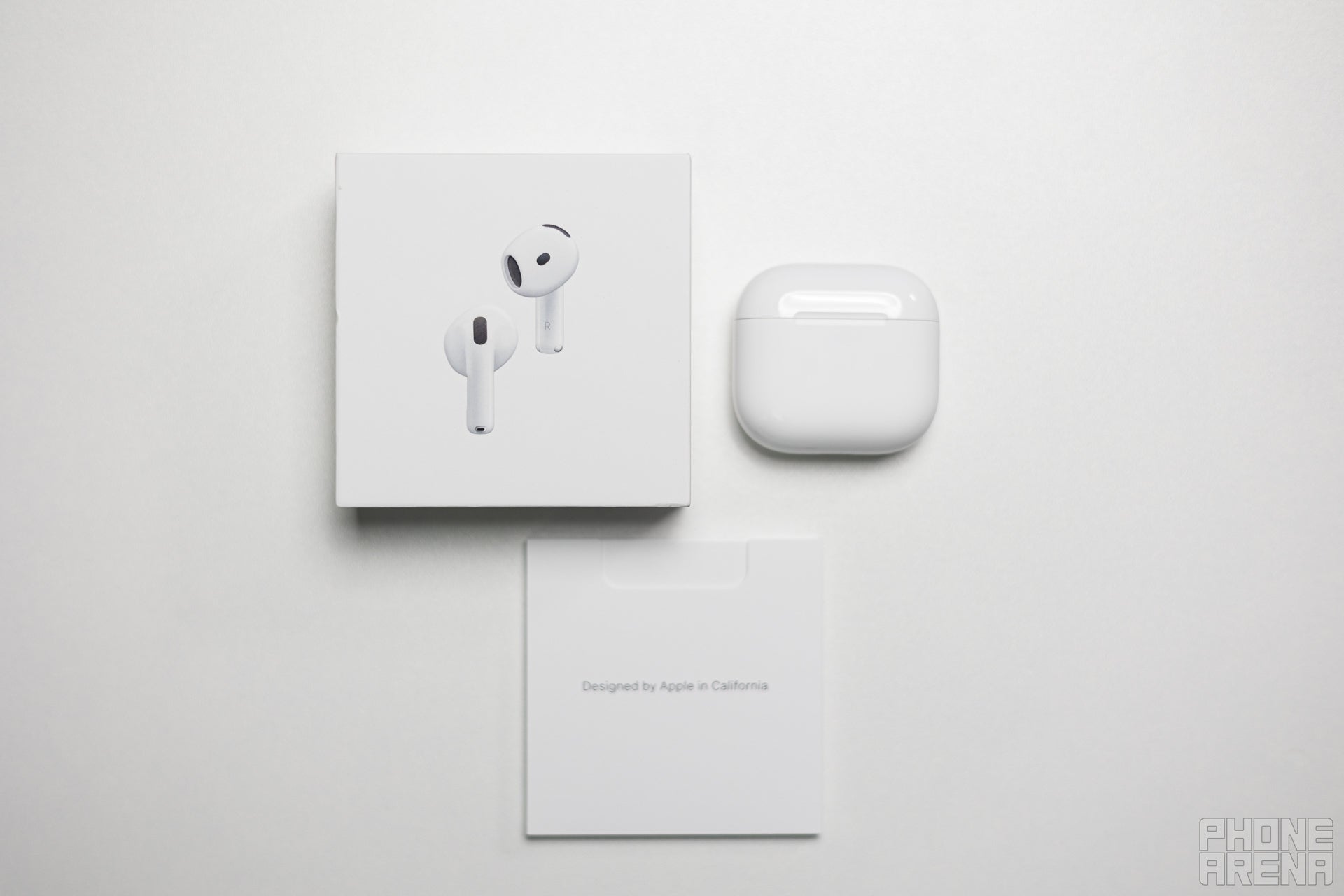 The box contents of the AirPods 4 — a booklet, the case with earbuds, and the box itself