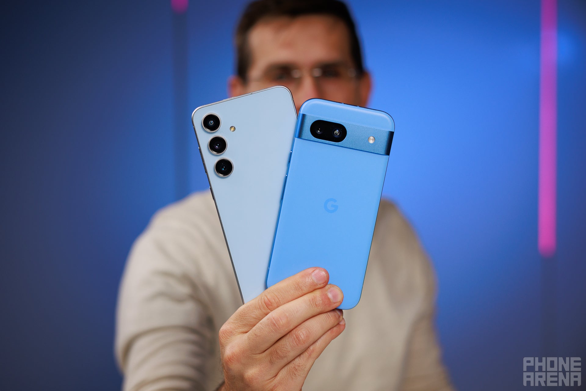 A man holding the Samsung Galaxy S24 FE next to the Google Pixel 8a