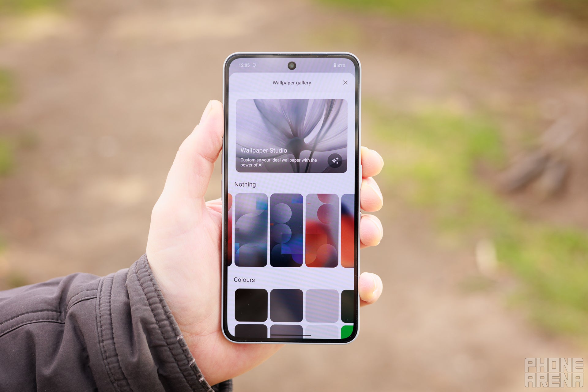 Hand holding Nothing Phone (3a) Pro towards the camera, screen is on showing the Settings screen for wallpaper selection