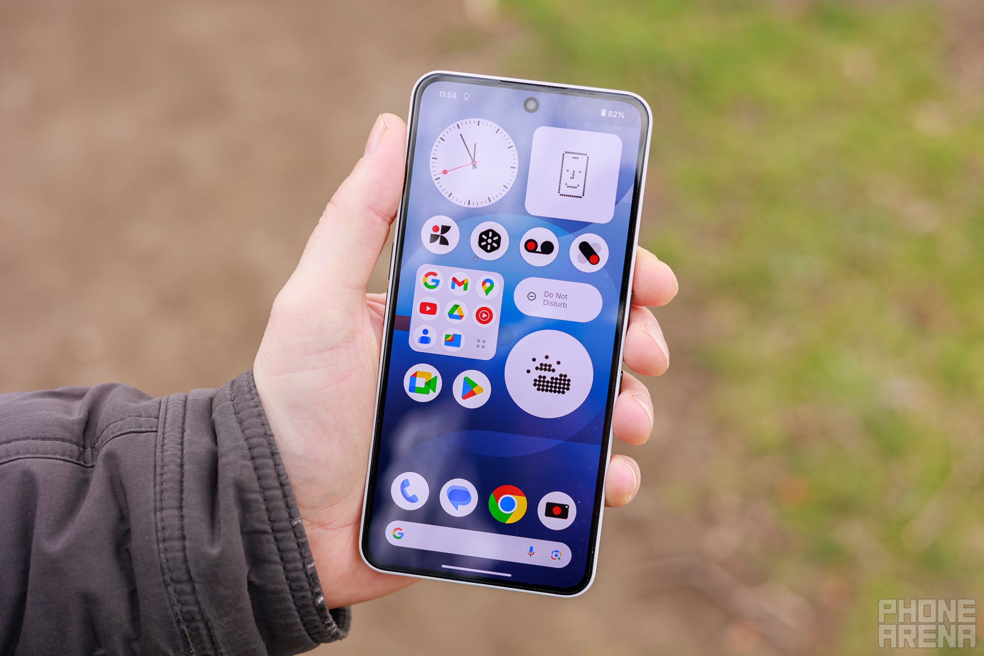 Hand holding Nothing Phone (3a) towards the camera, screen is on showing the first page of the homescreen