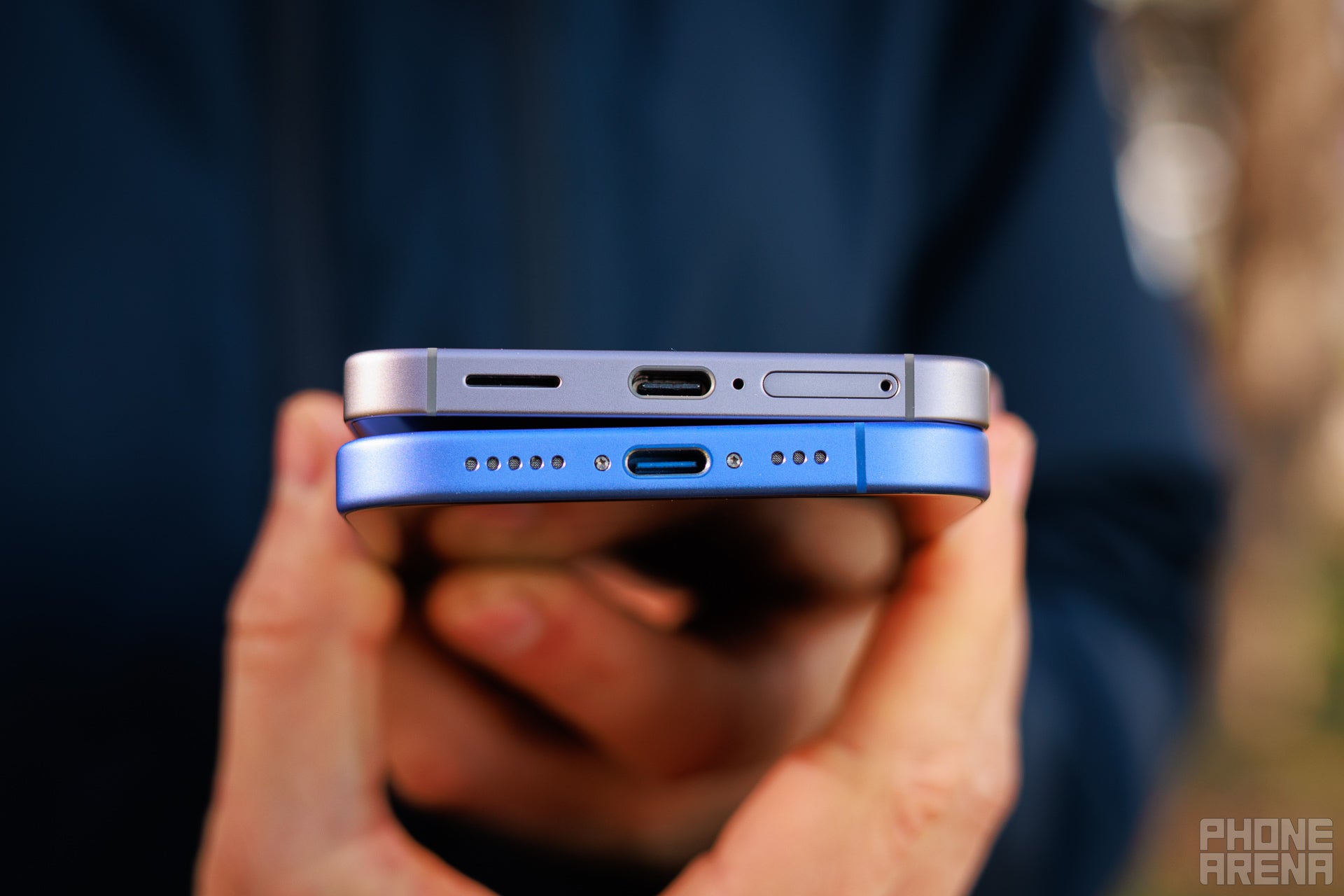 Hand holding both iPhone 16 and Galaxy S25 with their USB C ports towards the camera